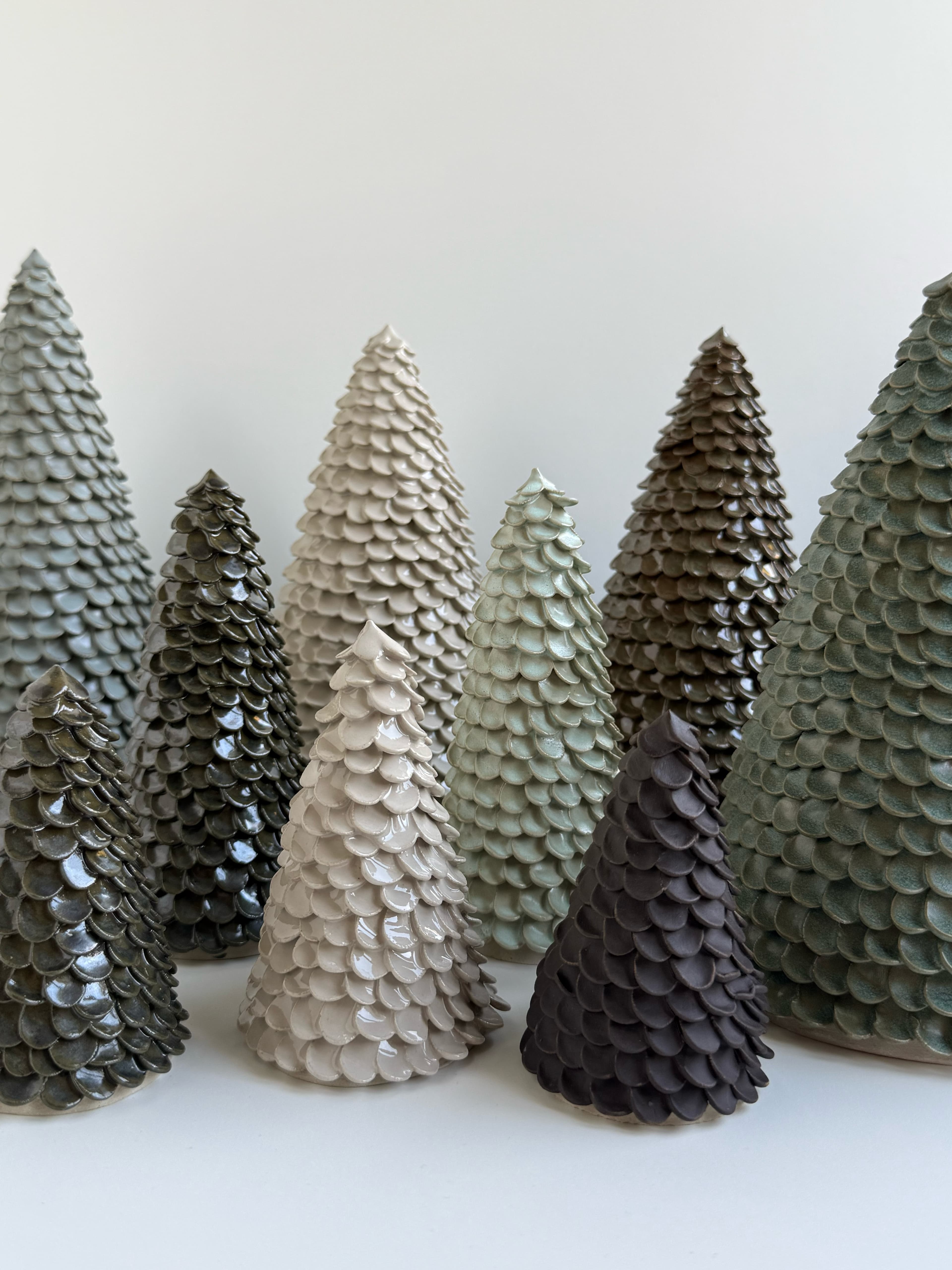 A close-up of handcrafted CLÆY ceramic trees in cream, pale green, grey and dark brown glazes