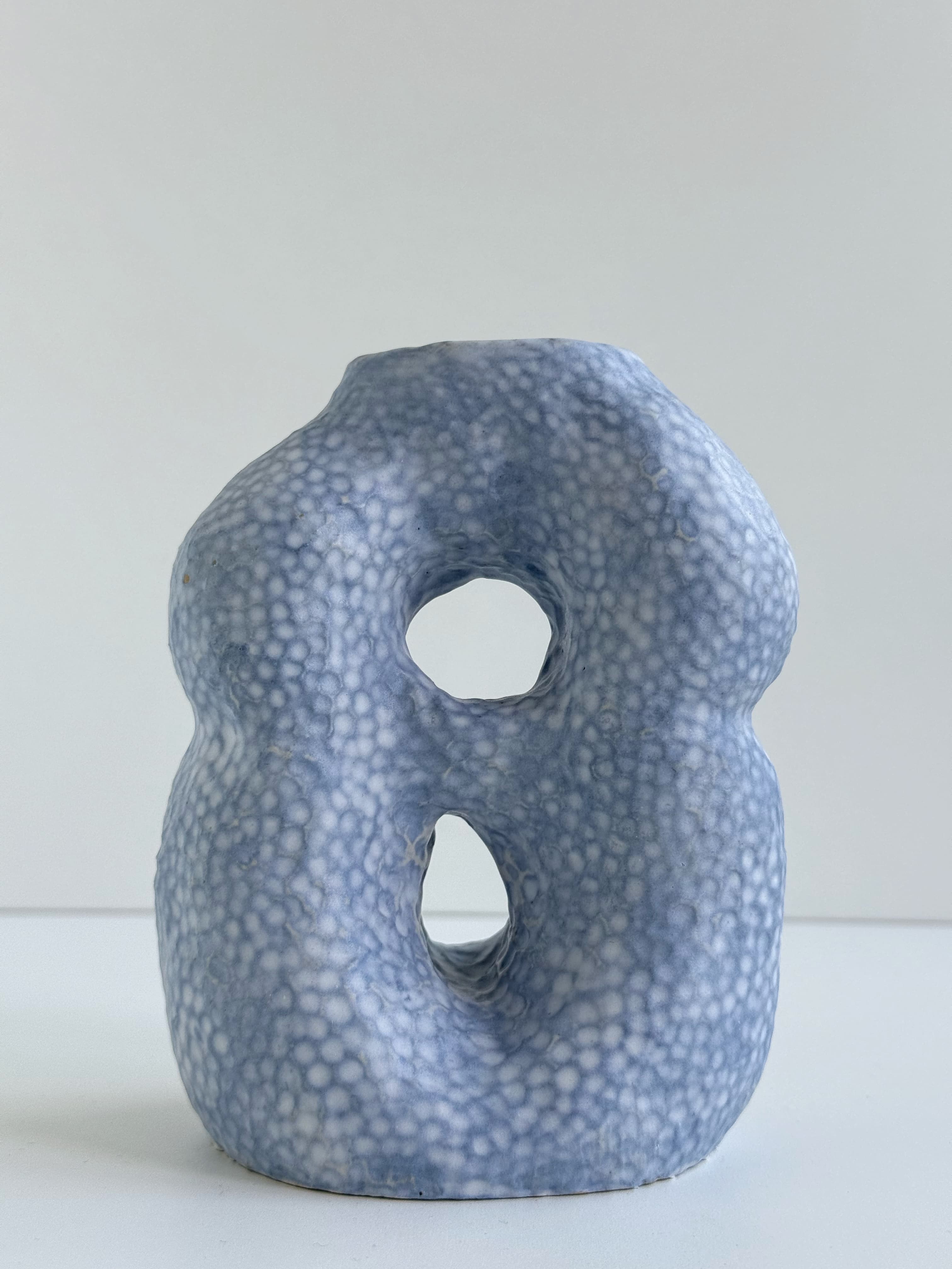 A blue-glazed CLÆY vessel with two openings and a dimpled surface