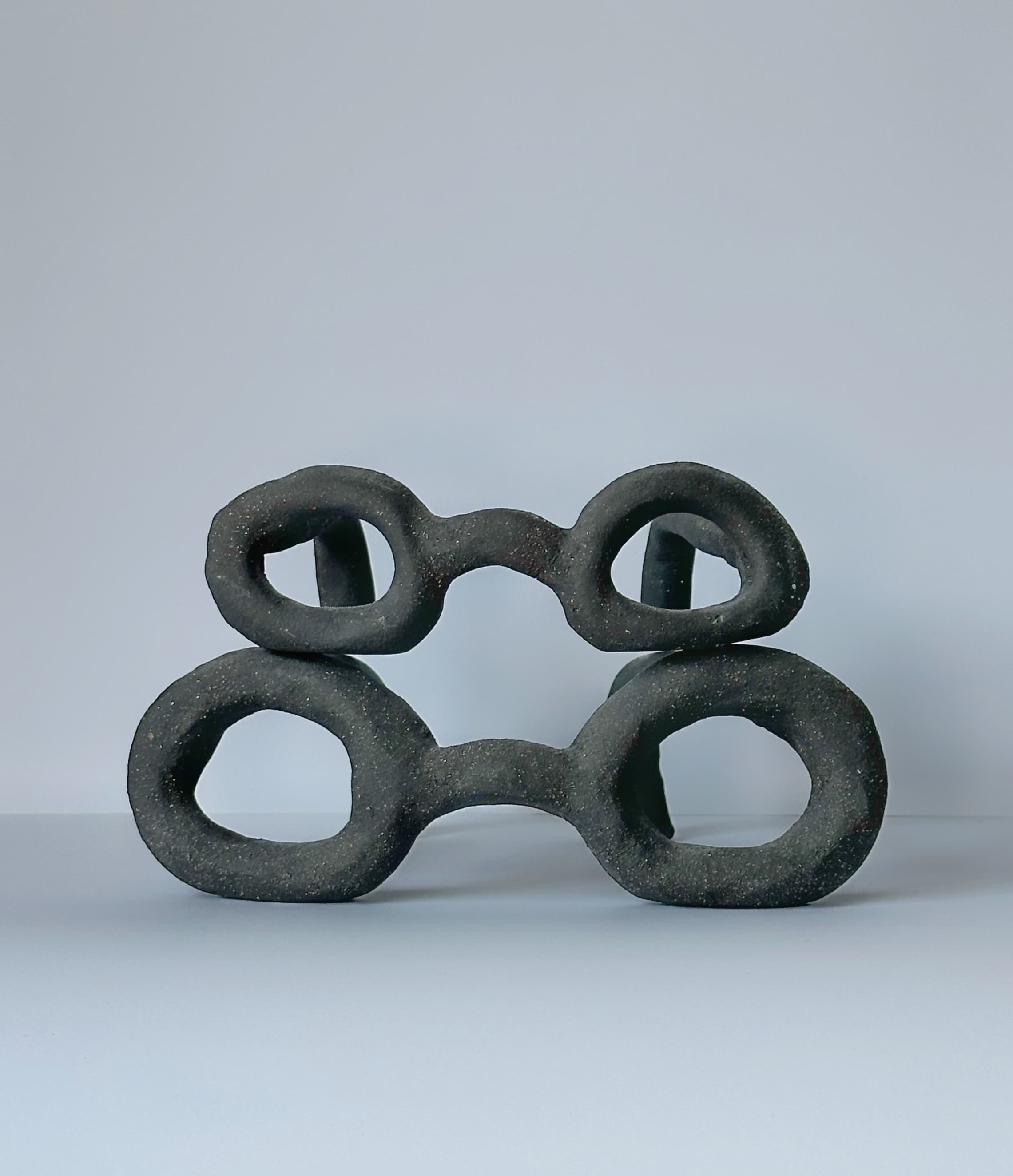 Two dark speckled CLÆY sculptures with paired openings, stacked on a pale surface